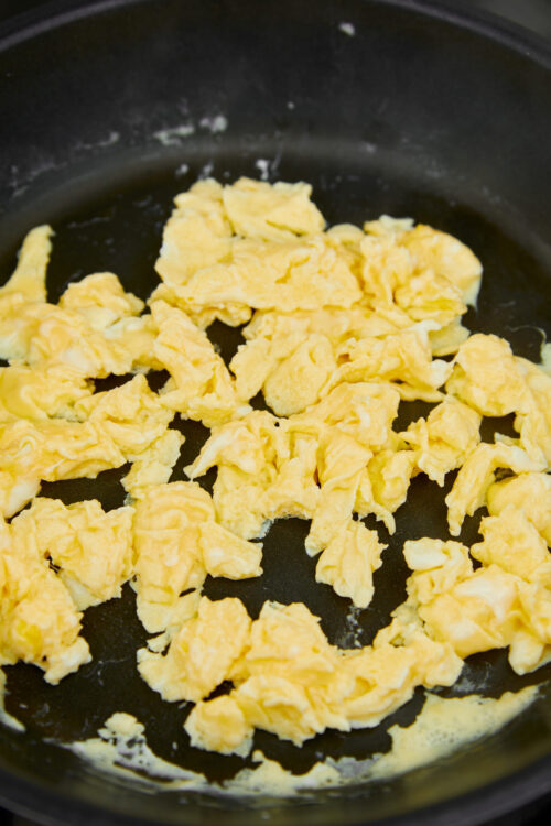 Fluffy scrambled eggs cooking in a black skillet for breakfast or brunch.