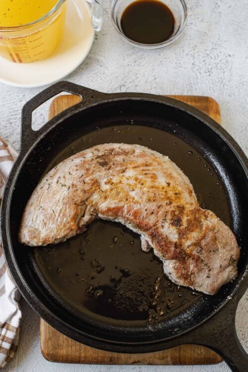 Juicy seared pork chop cooking in cast iron skillet on wooden board.