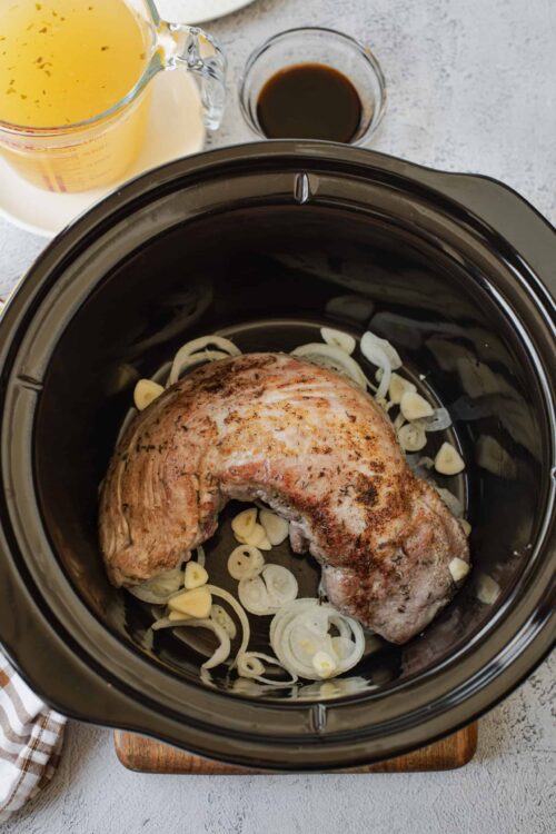 Slow cooker pork roast with sliced onions and garlic, ready for cooking in a modern slow cooker.