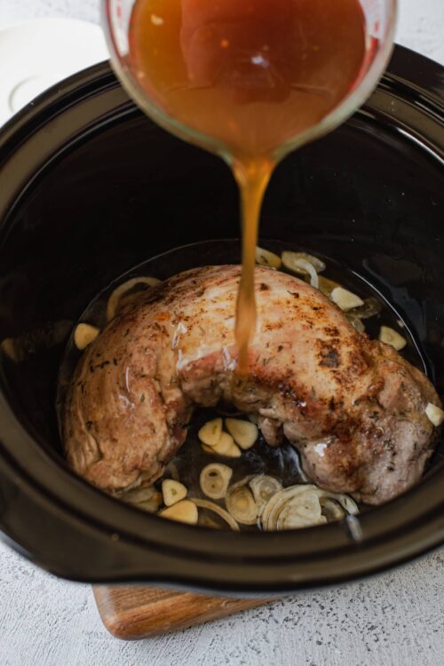 Juicy pork roast cooking in slow cooker with garlic and broth, ready for flavorful recipes.