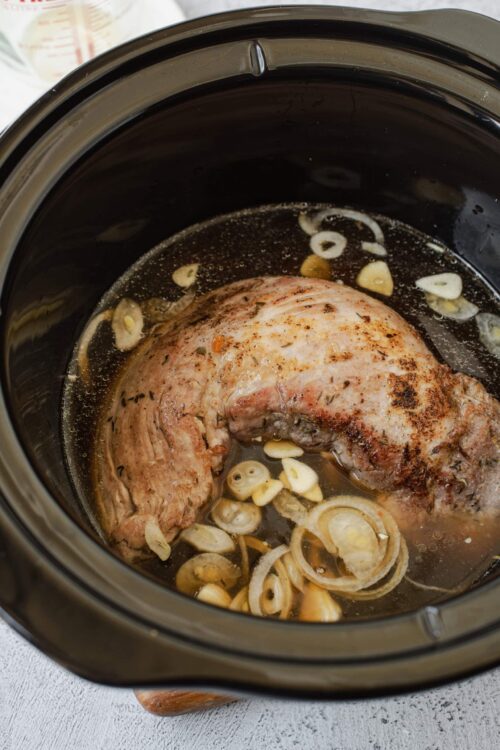 Seasoned pork roast with garlic and onion in a slow cooker for flavorful cooking.