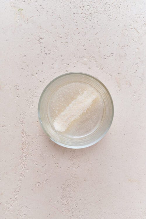 Fine sea salt in a clear glass bowl on a textured pink surface.