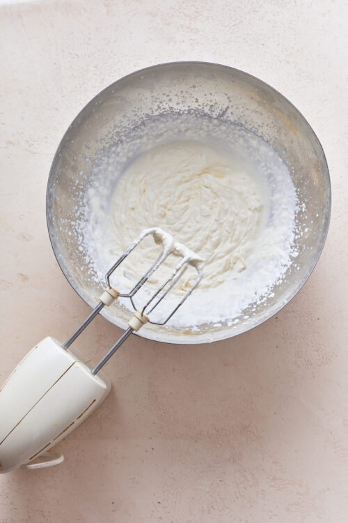 Fluffy whipped cream mixture in a metal bowl with hand mixer attached.