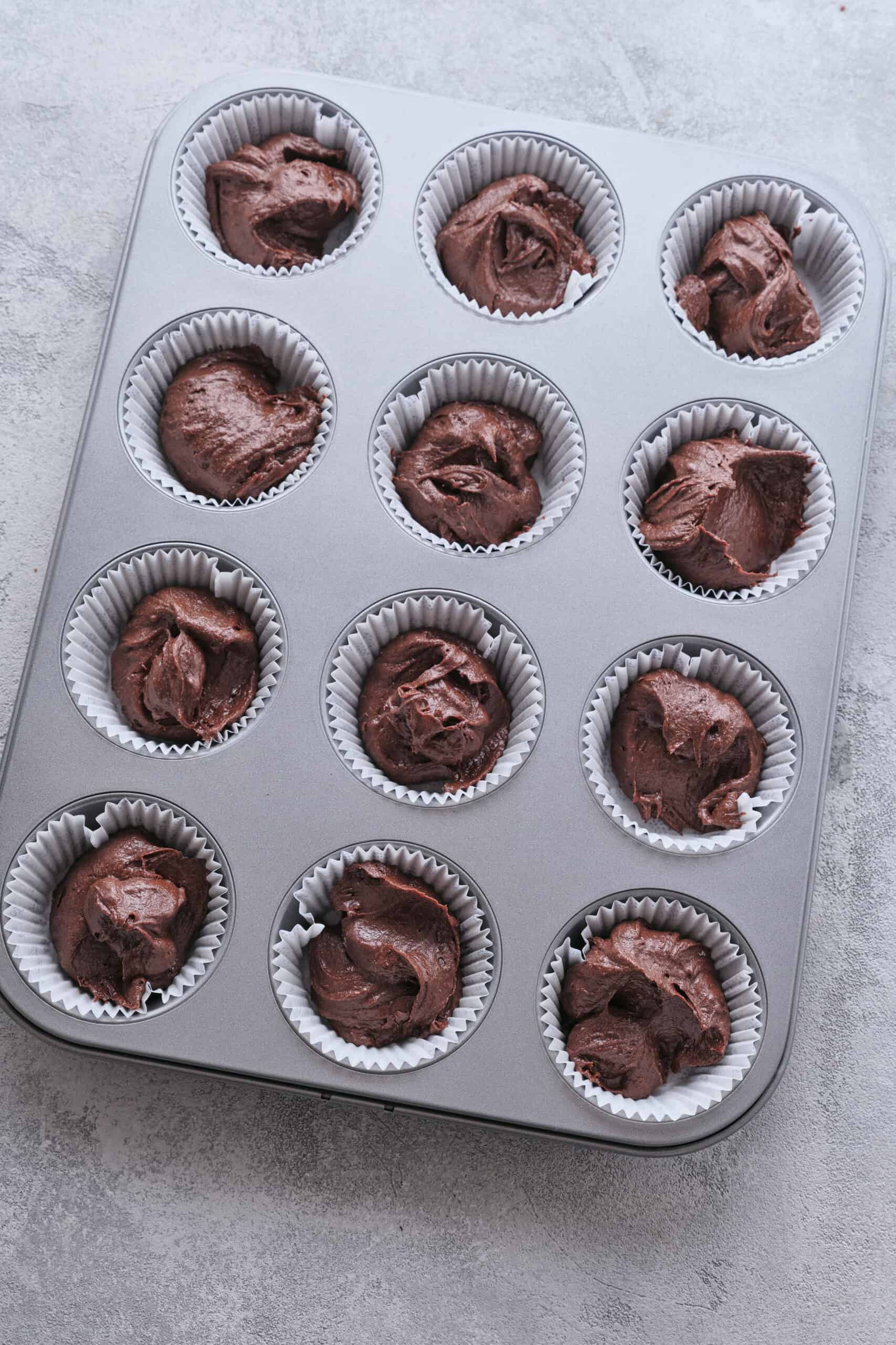 Rich chocolate cupcake batter in a cupcake tin with white paper liners.