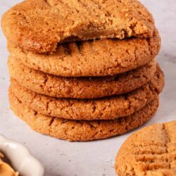 Chewy homemade peanut butter cookies stacked on a white surface.