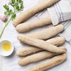 Fresh homemade breadsticks on parchment paper with garlic, parsley, and olive oil.