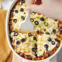 Cheesy baked casserole with black olives and green onions in a white dish.