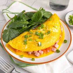 Fluffy breakfast omelette with ham and green onions on a white plate.