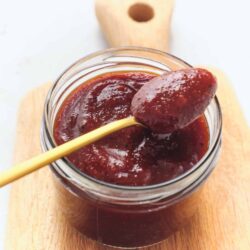 Sweet strawberry jam in a glass jar with a yellow spoon on a wooden board.