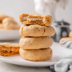 Soft homemade orange cookies with cream filling stacked on a white plate.