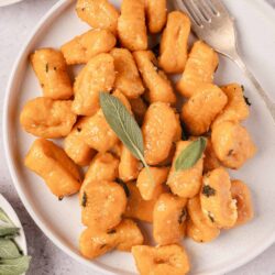 Golden pan-fried gnocchi on a white plate with sage leaves and black pepper, served with butter sauce.