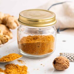 Ground spice blend in glass jar with nutmeg and cloves around, baking spices for cooking or baking, gourmet seasoning ingredients.