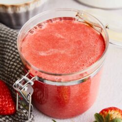 Fresh homemade strawberry smoothie in a glass jar with strawberries around it.