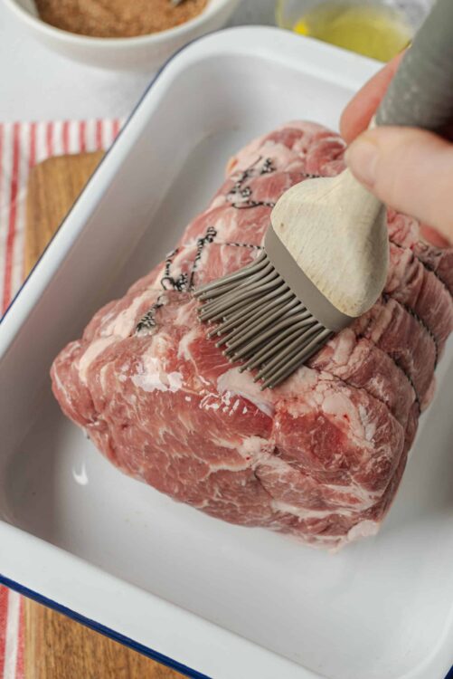 Raw beef roast being seasoned with an herb brush for a delicious baked meat recipe.
