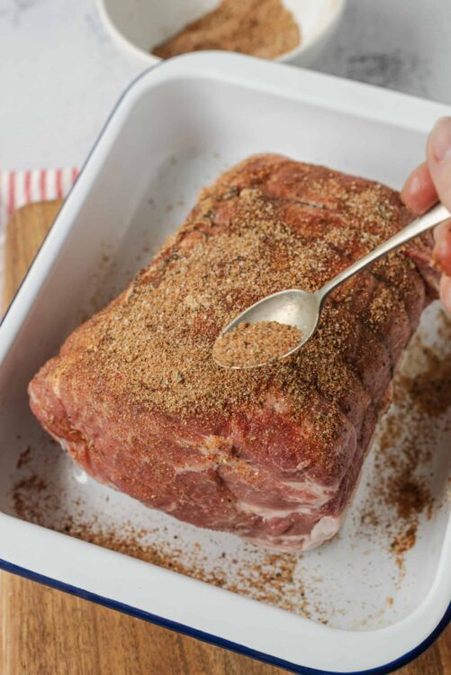 Seasoned beef roast being prepared for baking, with spices sprinkled on top.