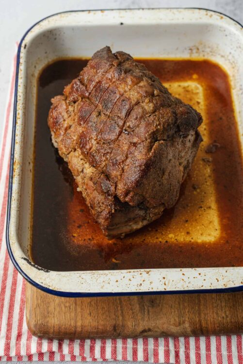 Juicy pot roast beef in a brown gravy in a white baking dish.