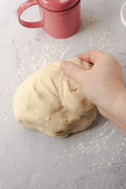 Soft bread dough resting on a floured surface with a pink mug in the background.