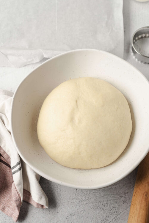 Soft risen pizza dough ball in a white bowl for homemade baking.