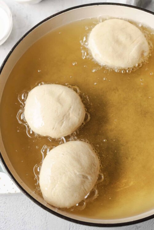 Fluffy bread rolls rising in hot oil during deep frying for homemade delicious bread.