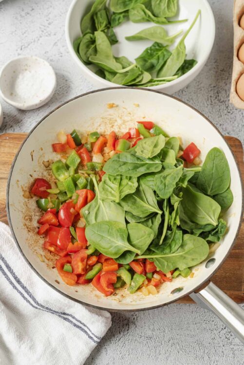 Fresh spinach and chopped vegetables cooking in a skillet, perfect for healthy recipes.