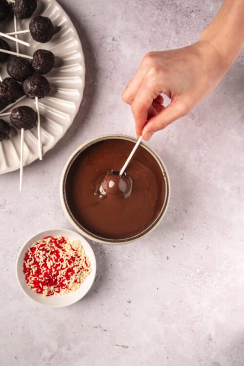 Decadent chocolate cake pops being dipped in melted chocolate with sprinkles and toppings.