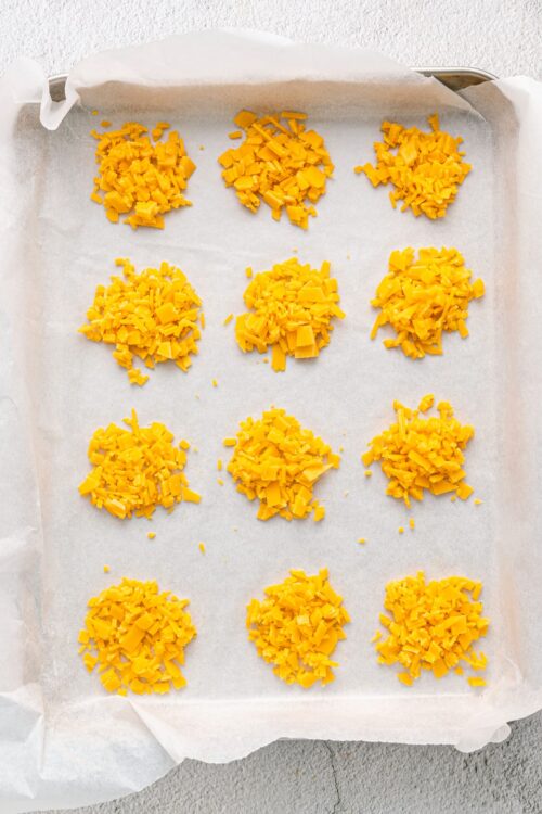 Shredded cheddar cheese spread on parchment paper for baking or cooking.