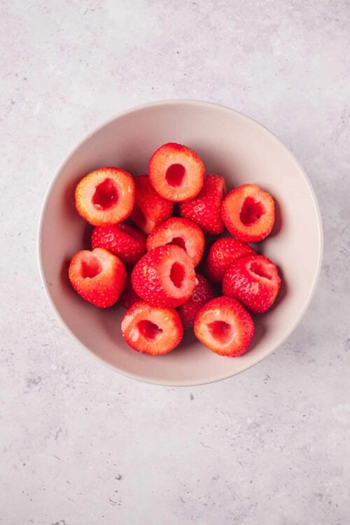 Fresh strawberries with a hollowed center in a white bowl on a light textured background.
