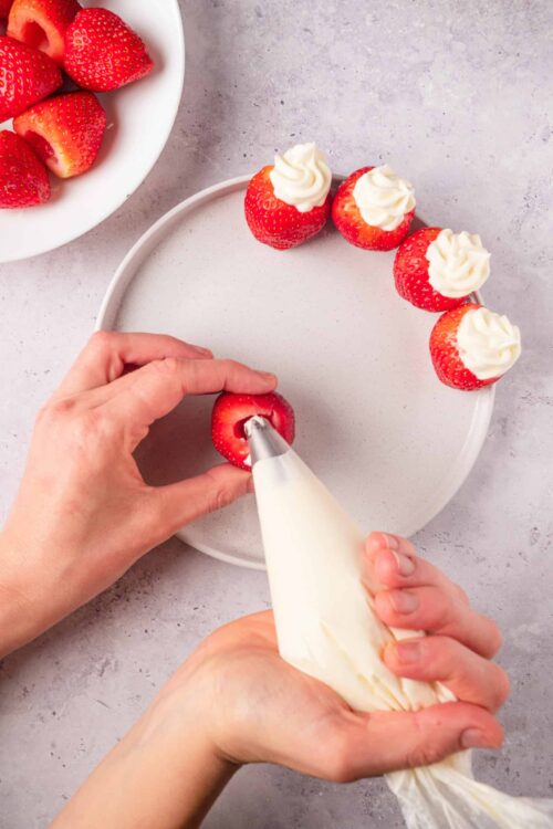 Fresh strawberries being filled with whipped cream for strawberry dessert bites.