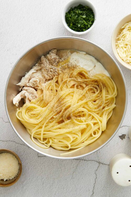 Creamy chicken Alfredo pasta dish with spaghetti, shredded cheese, and fresh herbs on a white background.