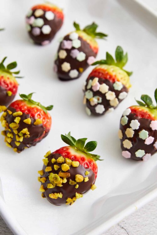 Chocolate dipped strawberries with colorful sprinkles and chopped nuts on a white platter.