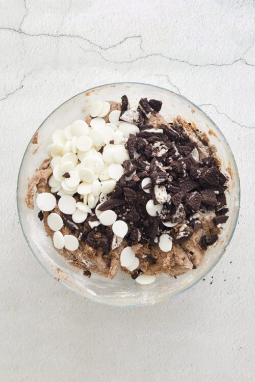 Chocolate chip cookie dough with white chocolate chips and crushed Oreo cookies in a glass mixing bowl.