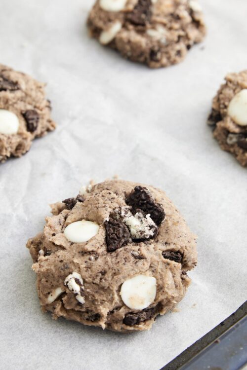 Chocolate chip cookie dough balls with white chocolate chunks on parchment paper.