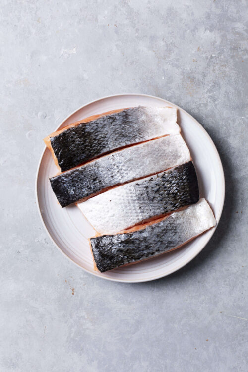 Fresh raw salmon fillets with skin on on a white plate, ready for cooking or baking.