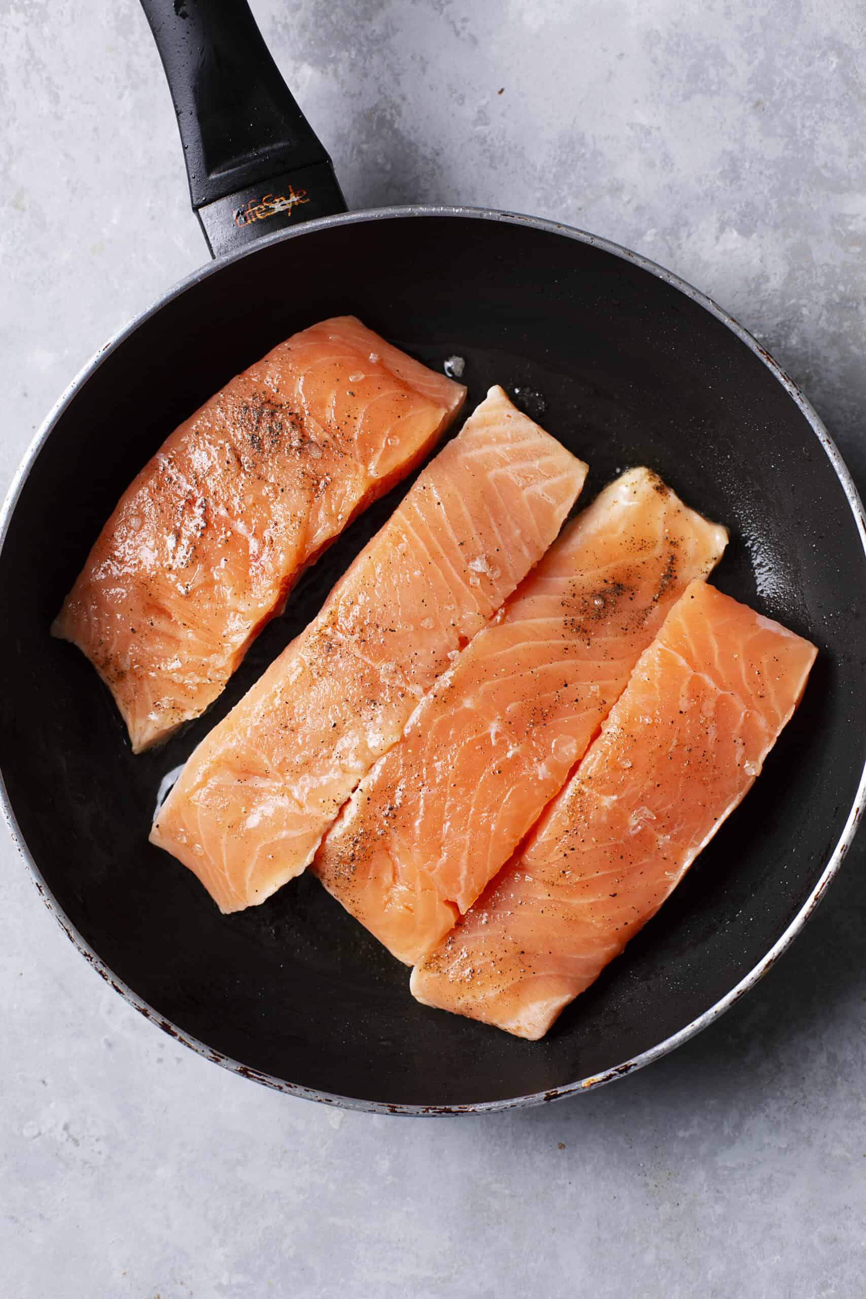 Salmon fillets cooking in a frying pan, seasoned and ready to cook.