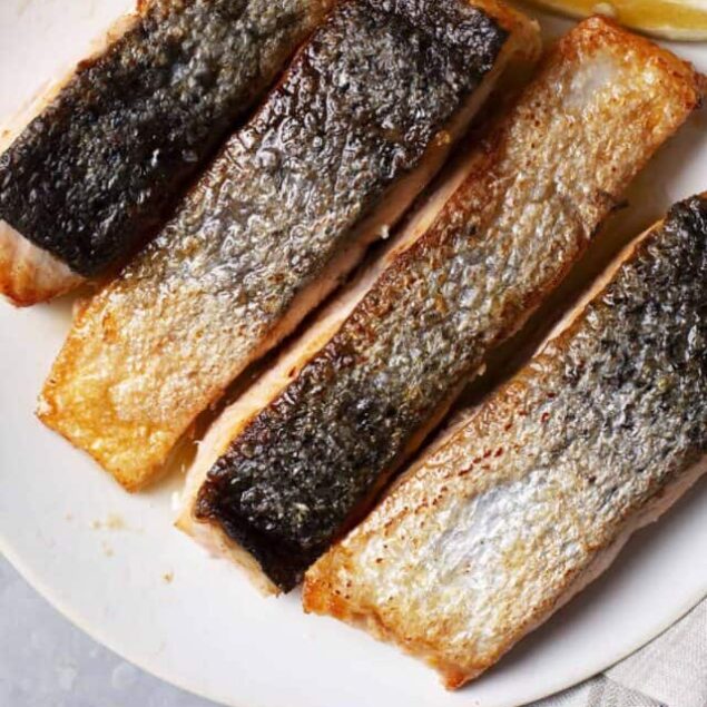 Golden crispy pan-seared salmon fillets with lemon wedges on a white plate.