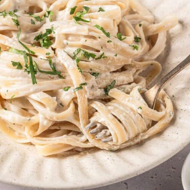 Creamy fettuccine alfredo pasta garnished with parsley on a rustic plate.