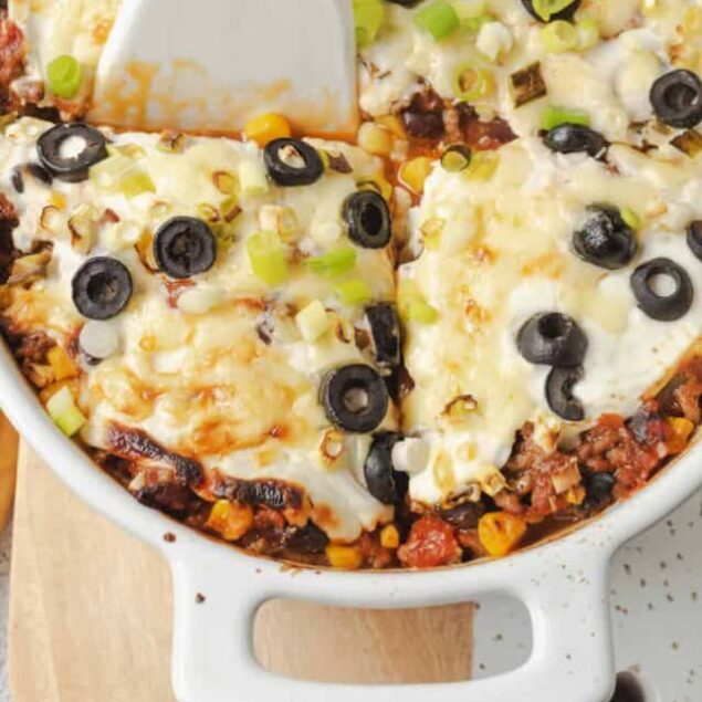 Cheesy baked casserole with black olives and green onions in a white dish.