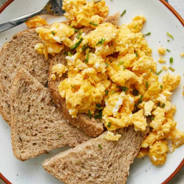 Fluffy scrambled eggs with whole wheat toast on a white plate.