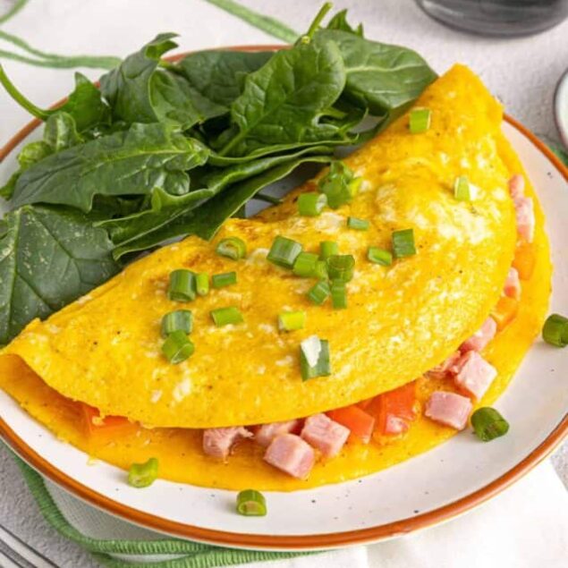 Fluffy ham and cheese omelette with fresh green onions and spinach on a white plate.