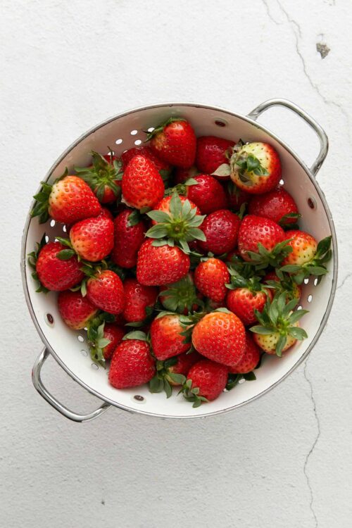 Fresh strawberries in a white metal colander for easy rinsing and serving.