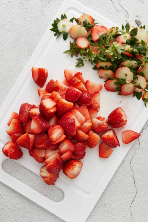 Sweet strawberries and sliced strawberries on white cutting board, fresh berry fruits for baking and desserts.