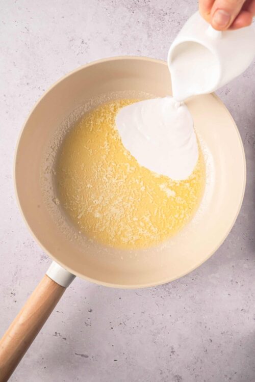 Buttermilk being poured into a mixing bowl with batter and shredded cheese, preparing for baking or cooking.