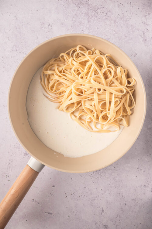 Creamy pasta with fettuccine and rich Alfredo sauce in a beige skillet, perfect for comfort food recipes.