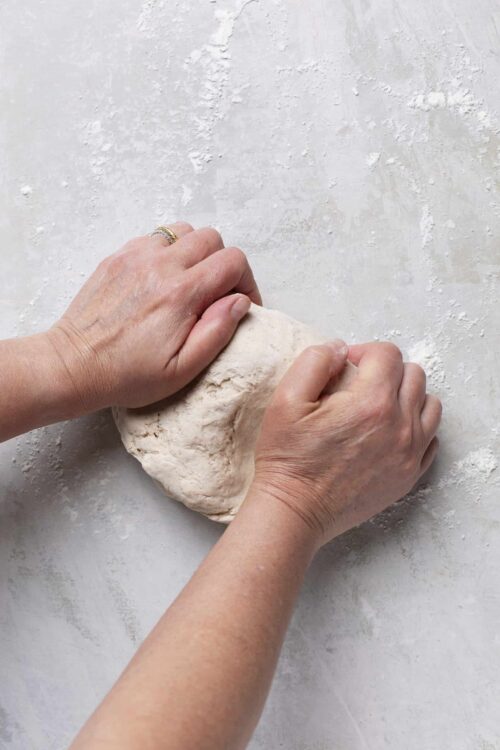 Soft bread dough being kneaded on a floured surface.