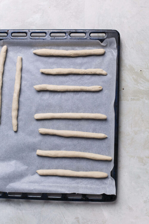 Raw unbaked breadsticks on baking sheet.