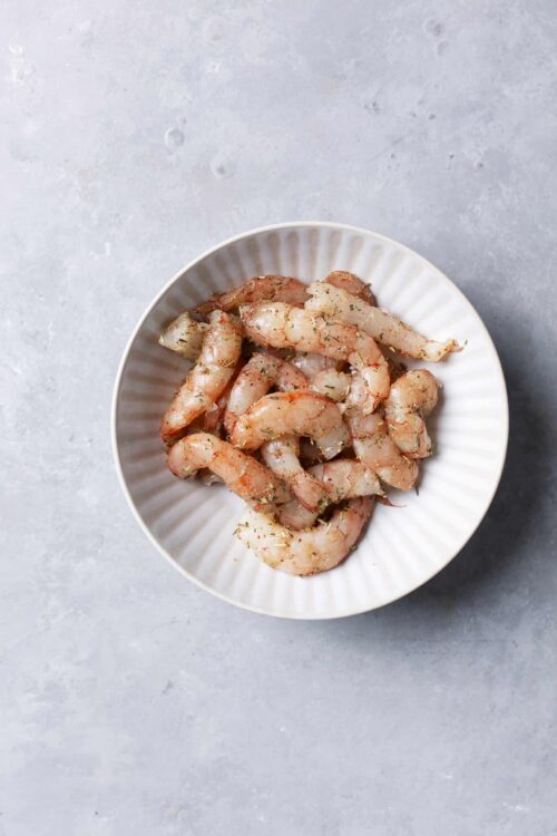 Raw shrimp with herbs on a white plate for cooking or recipe ingredients.