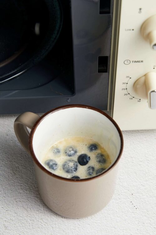 Fresh blueberry pancake batter in a mug on a kitchen counter.