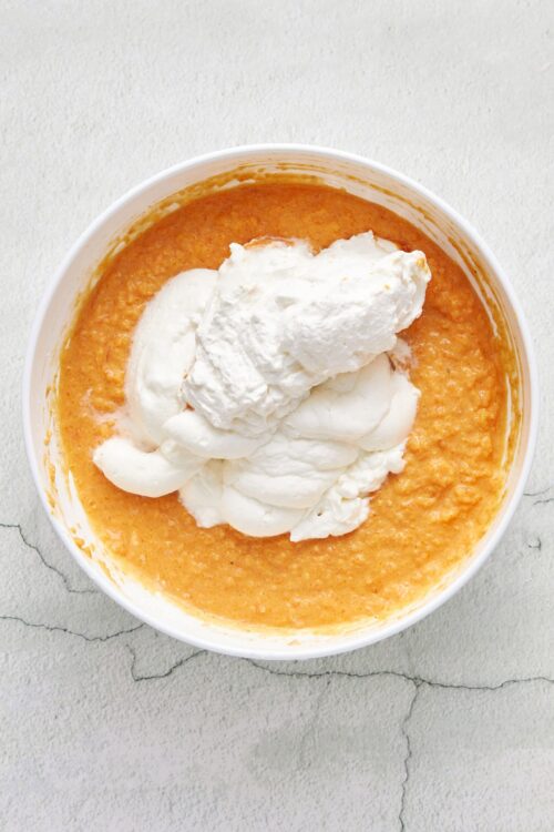 Creamy butternut squash soup topped with dollops of whipped cream on a white textured background.