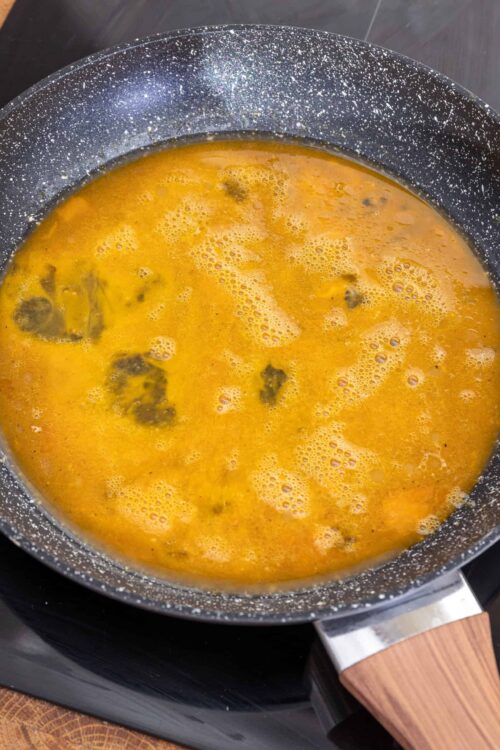 Boiled eggs cooking in a speckled non-stick skillet on stovetop.
