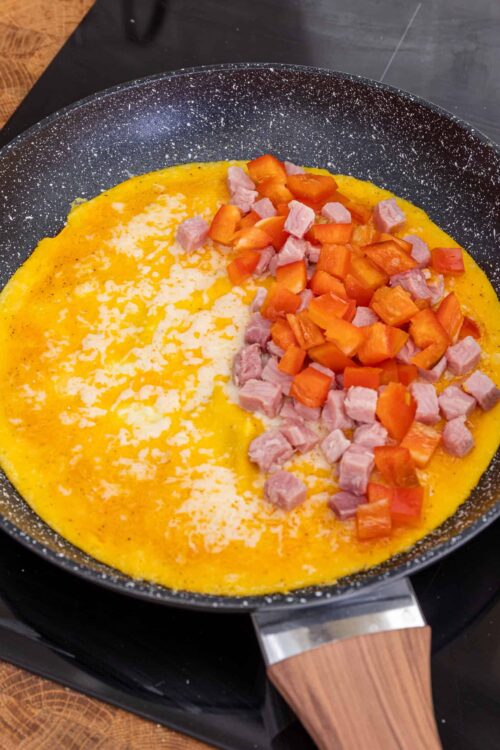 Creamy scrambled eggs with diced ham and bell peppers in a non-stick skillet. Perfect for breakfast or brunch.